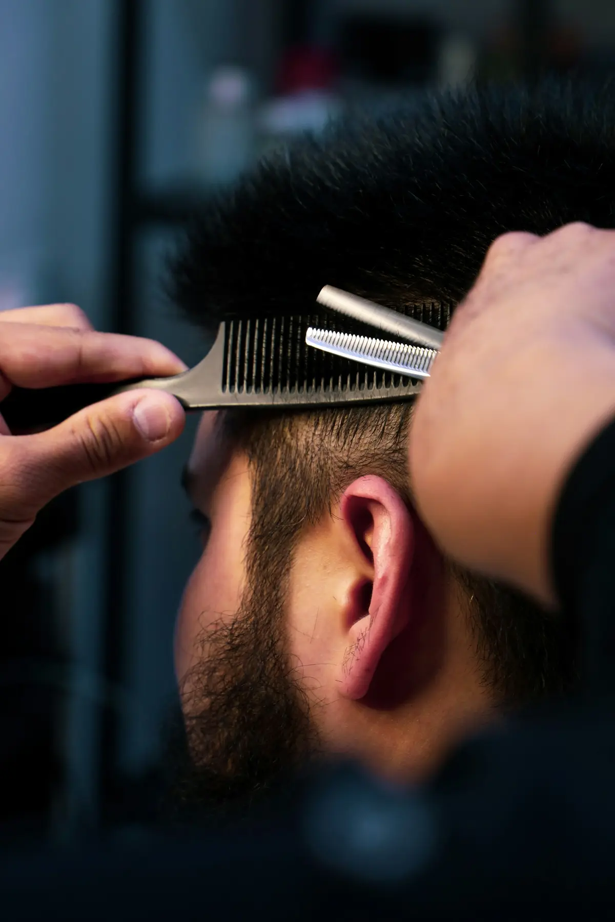 Nahaufnahme: Friseurhände führen Effilierschere und Kamm durch kurzes dunkles Haar (Symbolbild)